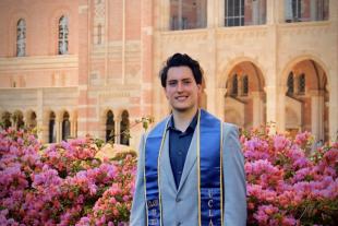 Gabe Fernandez standing in a garden on UCLA campus, wearing a graduation stole