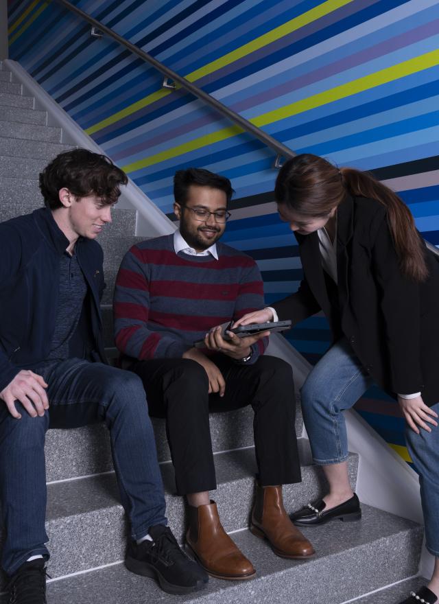 Group of individuals sitting on stairs looking at a tablet