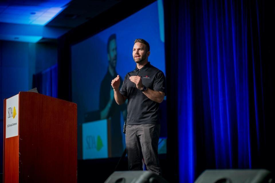 Mac Clemmens speaking on stage, behind a podium