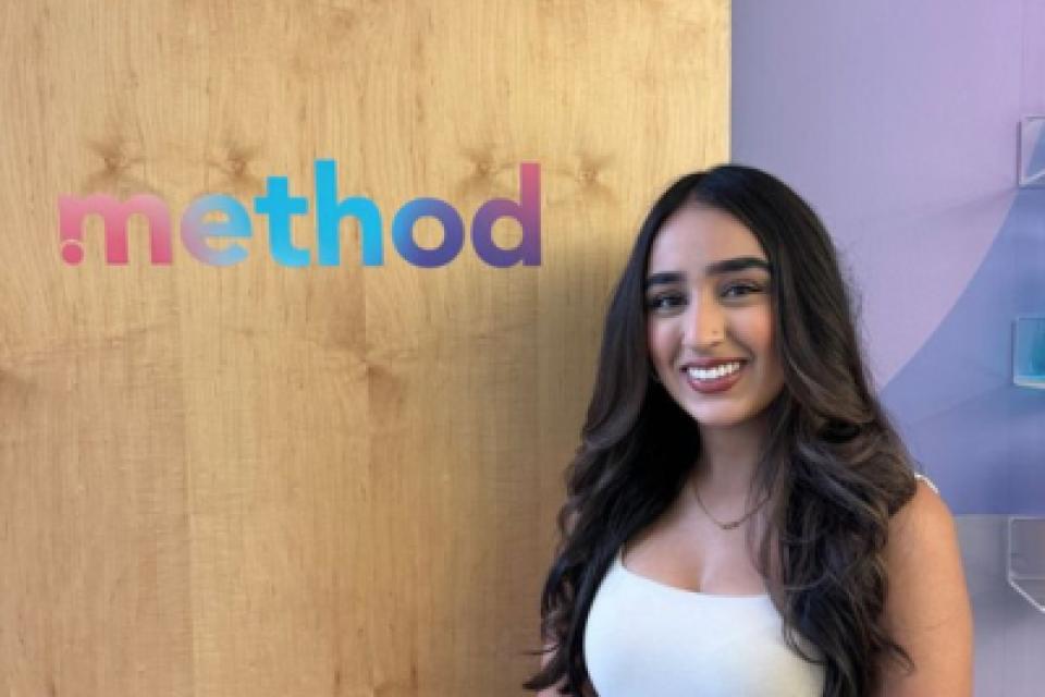 Simrun Bhandal standing in front of a wooden wall with the logo 'method' in colorful text.